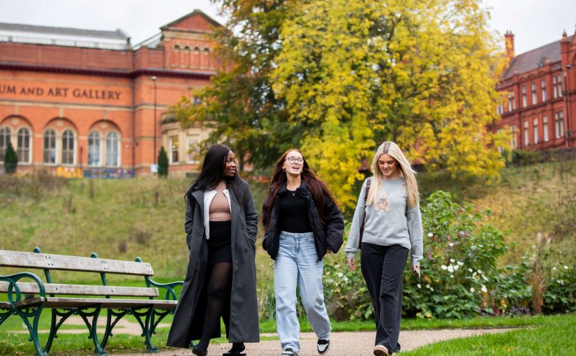 Three students walking through Peel Park on a sunny day.