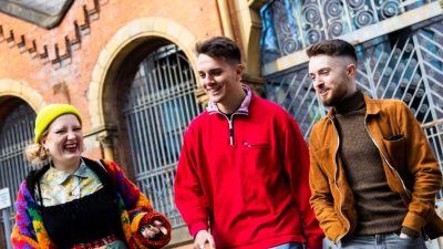 Three students laughing and walking outside in Manchester City