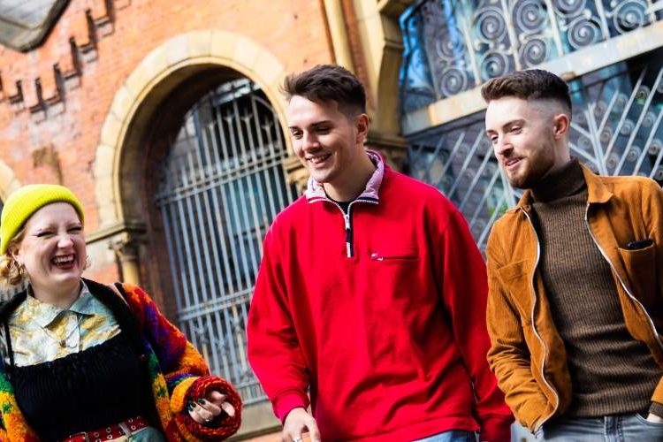 Three students laughing and walking outside in Manchester City
