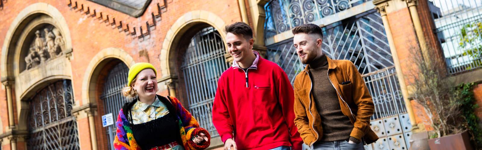 Three students laughing and walking outside in Manchester City