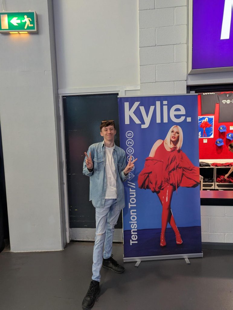 Josh standing next to a Kylie Minogue pull-up banner.