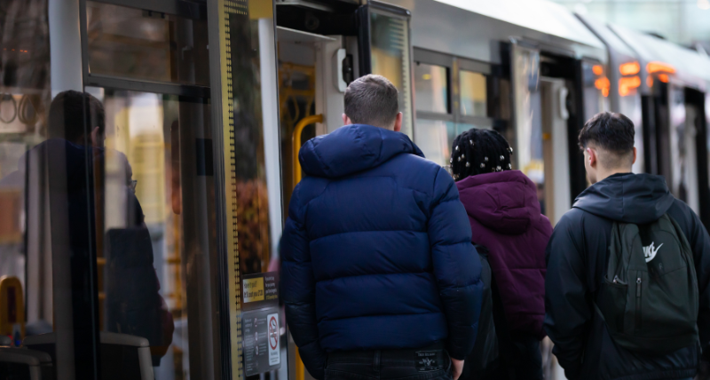 Three three students board a tram at Salford Quays.