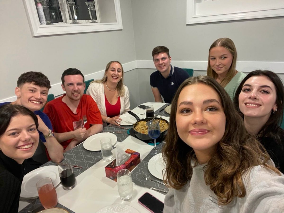 A group of eight friends sat around a table smiling at the camera