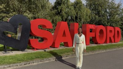 Student standing in front of main Salford sign