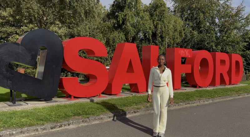 Student standing in front of main Salford sign