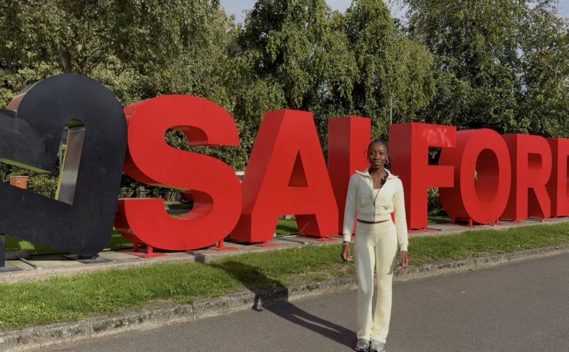 Student standing in front of main Salford sign