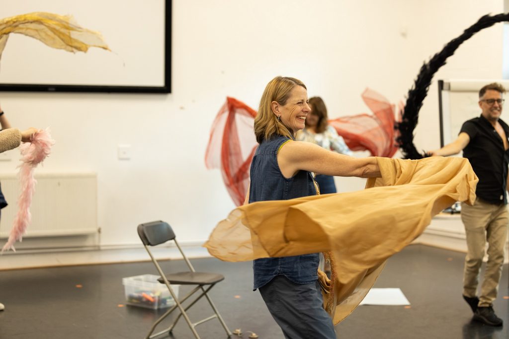 Three people taking part in a workshop dancing and waving around colourful scarves